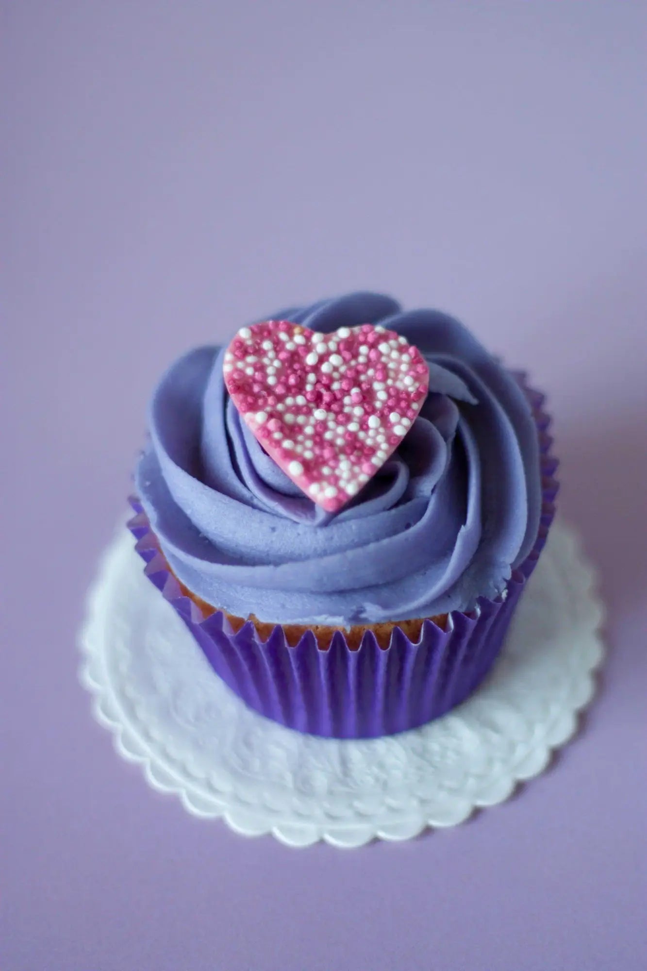 Lavender-frosted cupcake with pink heart-shaped sprinkle decoration in a baking professional collection