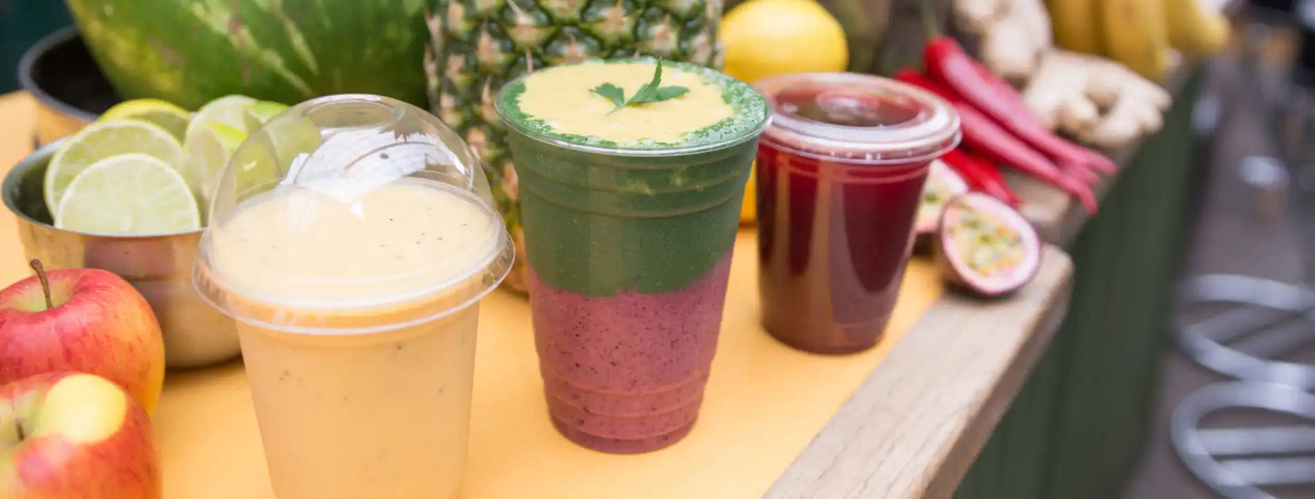 Three colorful layered smoothies in clear plastic cups with domed lids.